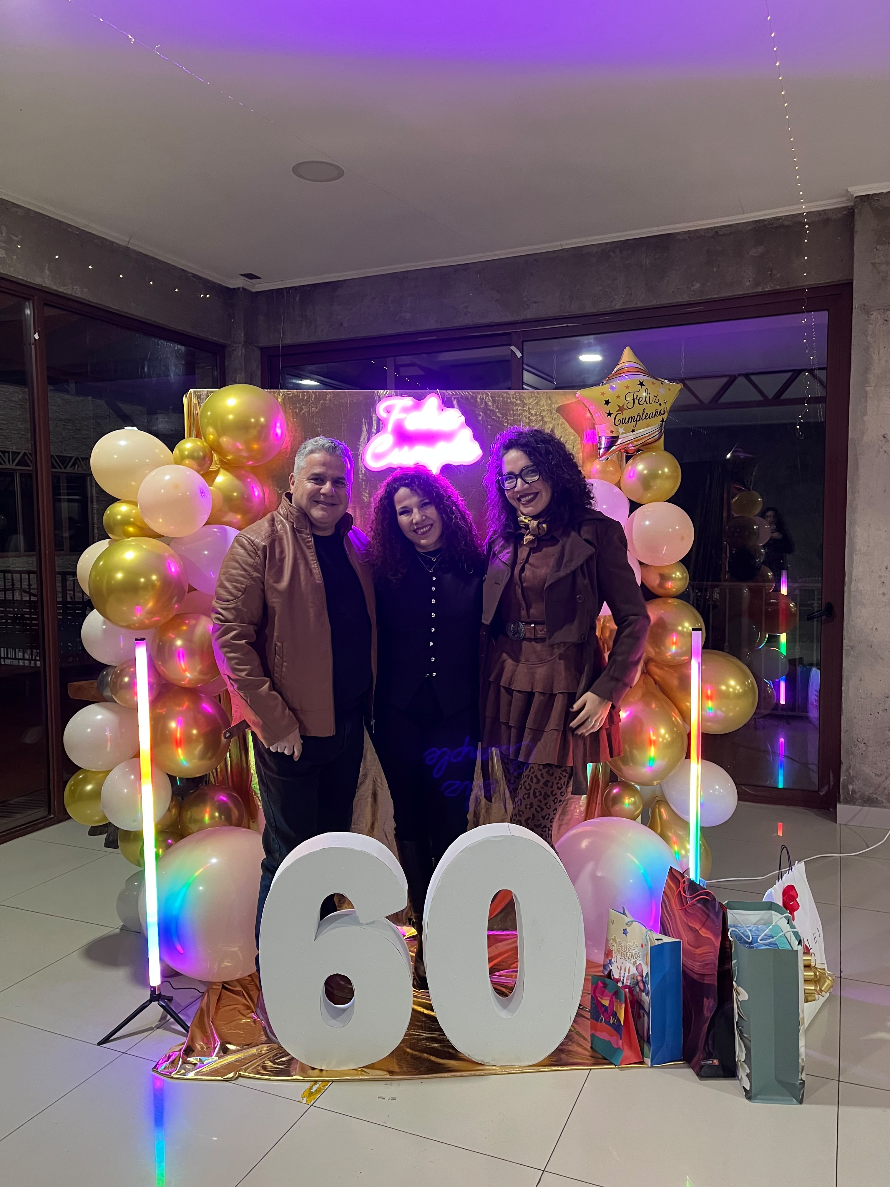 Eli acompañada por dos invitados frente a la decoración